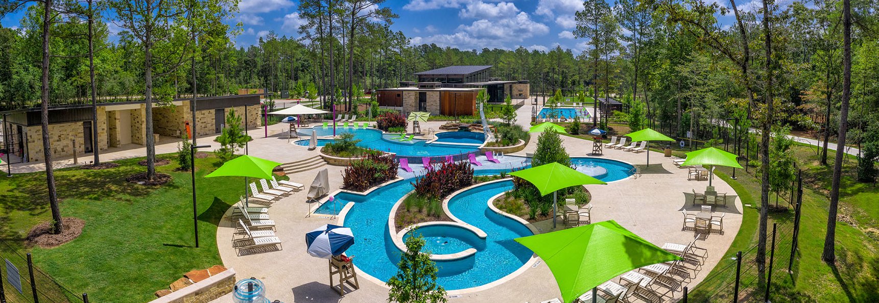 Community pool with winding blue water, green shade canopies, and a wooded clubhouse setting.