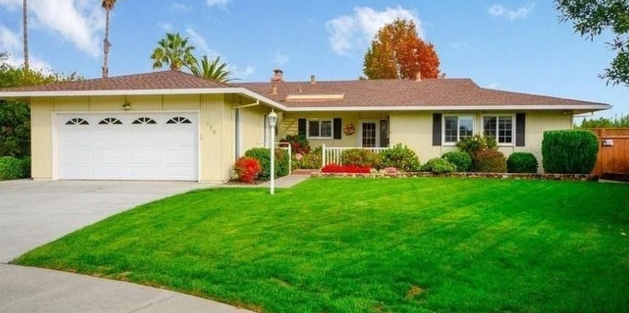 Single-story ranch home with an attached garage, broad green lawn, and landscaped front yard.
