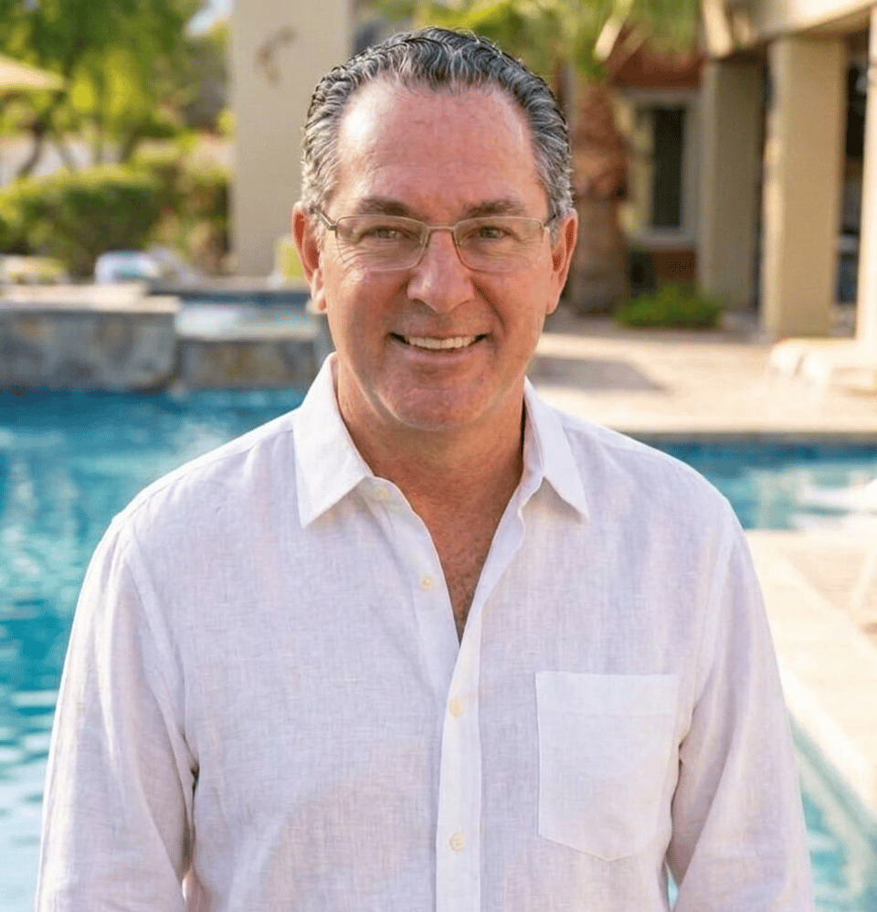 Smiling man in glasses and a white shirt beside a swimming pool.