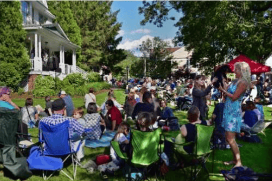 People gather outdoors for a summer music event on a grassy lawn.