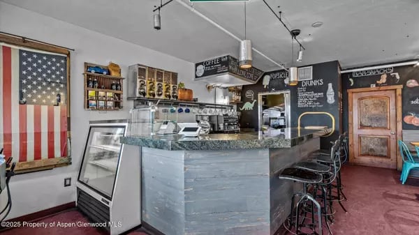 Café counter with espresso equipment, bar stools, menu boards, and an American flag in the window.