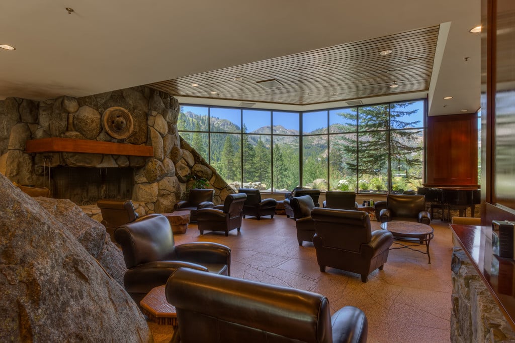 Resort lounge with a stone fireplace, leather chairs, and mountain views through expansive windows.
