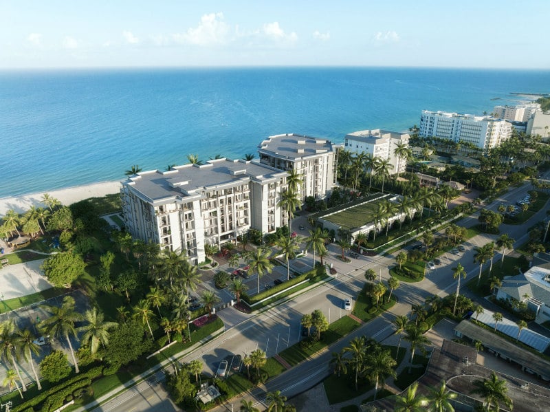Aerial rendering of modern condominium buildings beside a sandy beach and palm-lined streets.