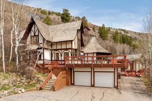 Tudor-style mountain home with a raised deck, steep roofs, and two garage doors.
