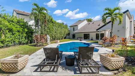 Backyard pool with two lounge chairs, tropical landscaping, and the rear of a light-colored home.
