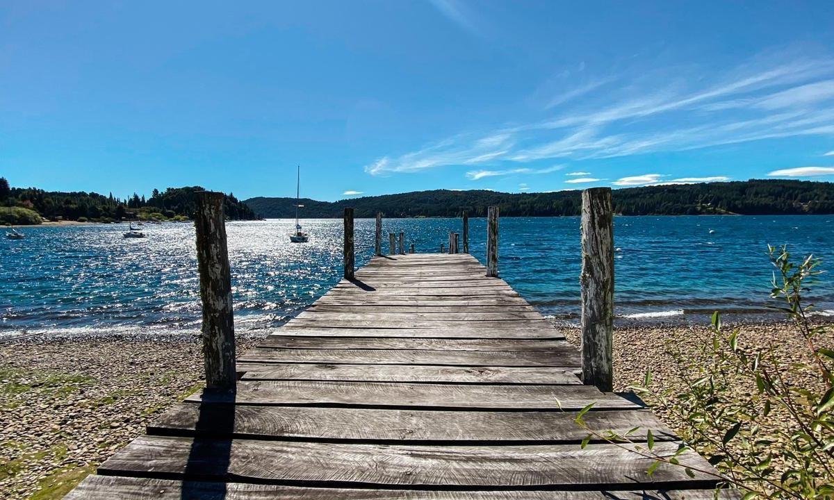 Wooden dock extending into a blue lake, with sailboats and wooded hills beyond.