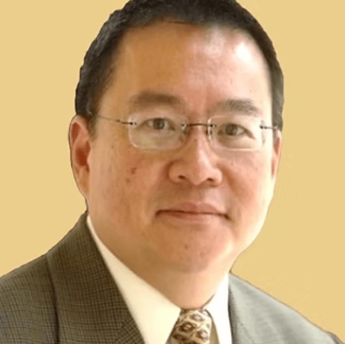 Man wearing glasses, a checked suit jacket, and patterned tie.