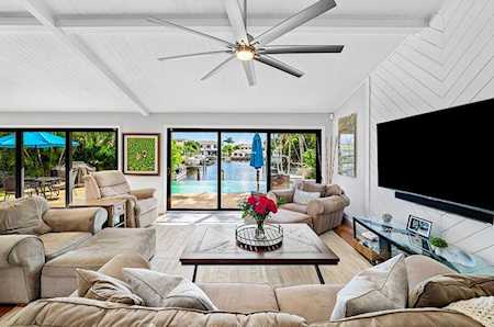 Living room with a vaulted ceiling and wide windows overlooking a pool and tropical landscaping.