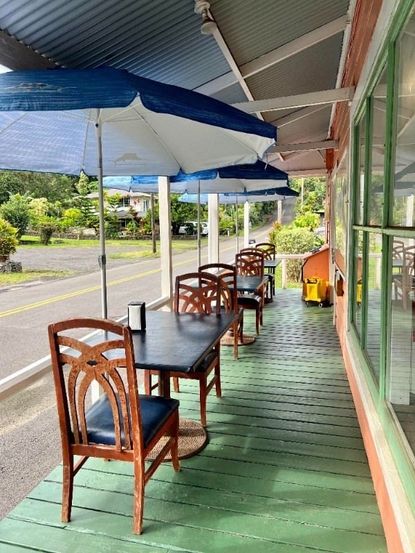 Commercial storefront porch with wooden tables and chairs beneath blue-and-white umbrellas.