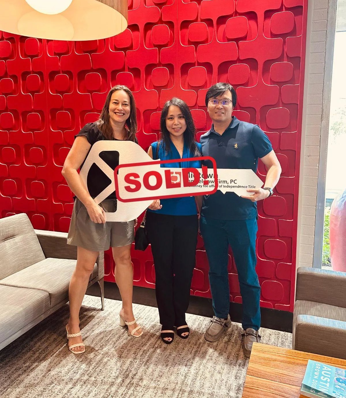 Three adults pose with a large key-shaped sign under a red SOLD stamp.