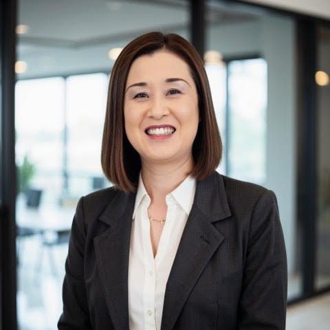 Keiko Mabuchi smiling in a dark blazer and white blouse in an office.