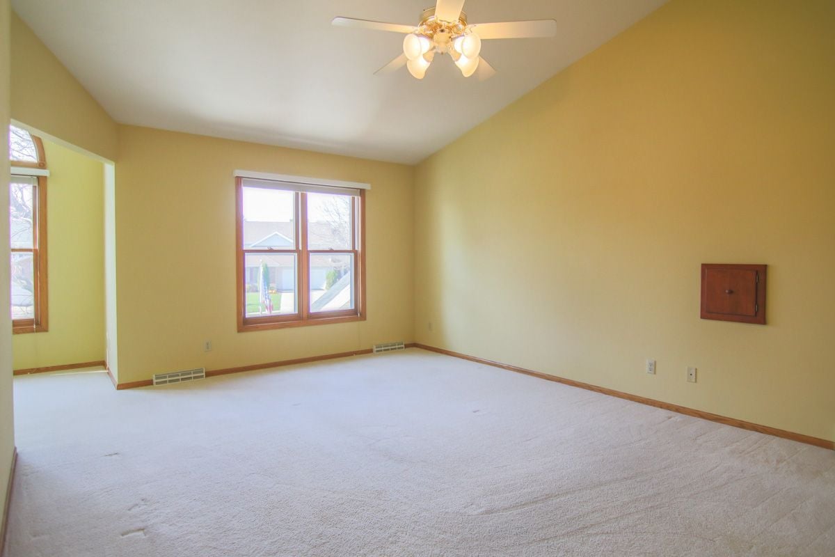 Empty room with pale carpet, yellow walls, two windows, and a ceiling fan with lights.