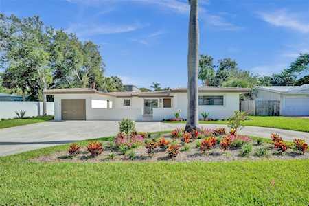Single-story white home with an attached garage, flower garden, and palm tree in front.