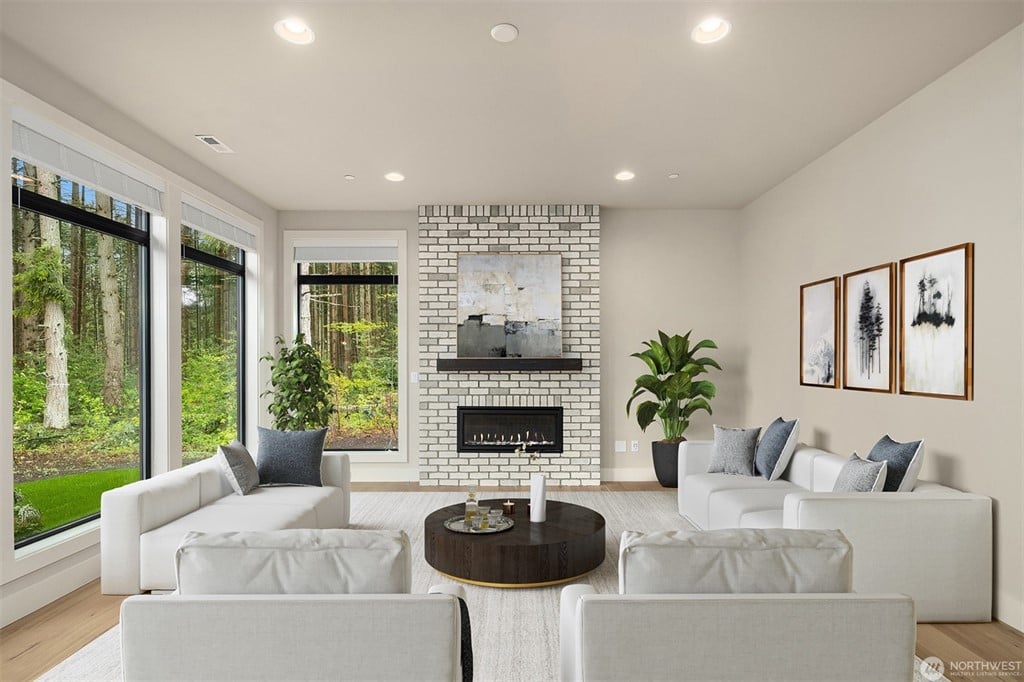 Spacious modern living room featuring floor-to-ceiling windows with forest views, white brick fireplace, contemporary white furniture, and natural light, perfect feature in luxury homes.