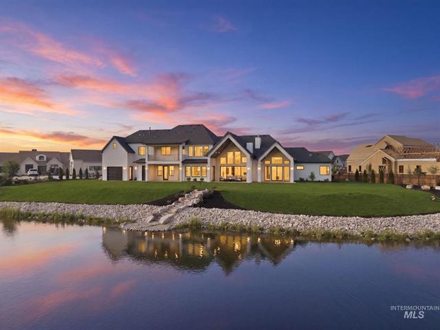 Waterfront home with illuminated windows and a stone path beside the water at sunset.