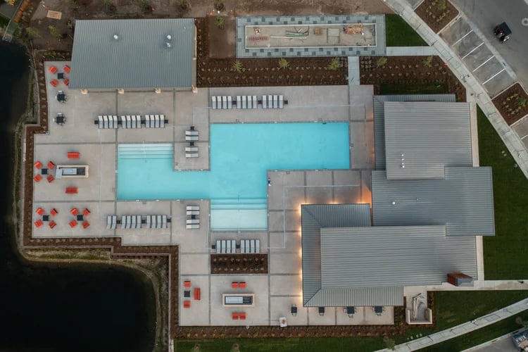 Aerial view of a community swimming pool with lounge chairs and covered facilities beside a pond.