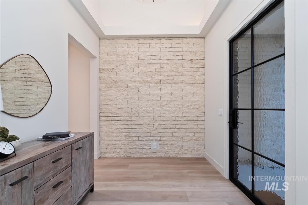 Entry with black steel and glass front door, white stone accent wall, high ceiling, and white oak floor
