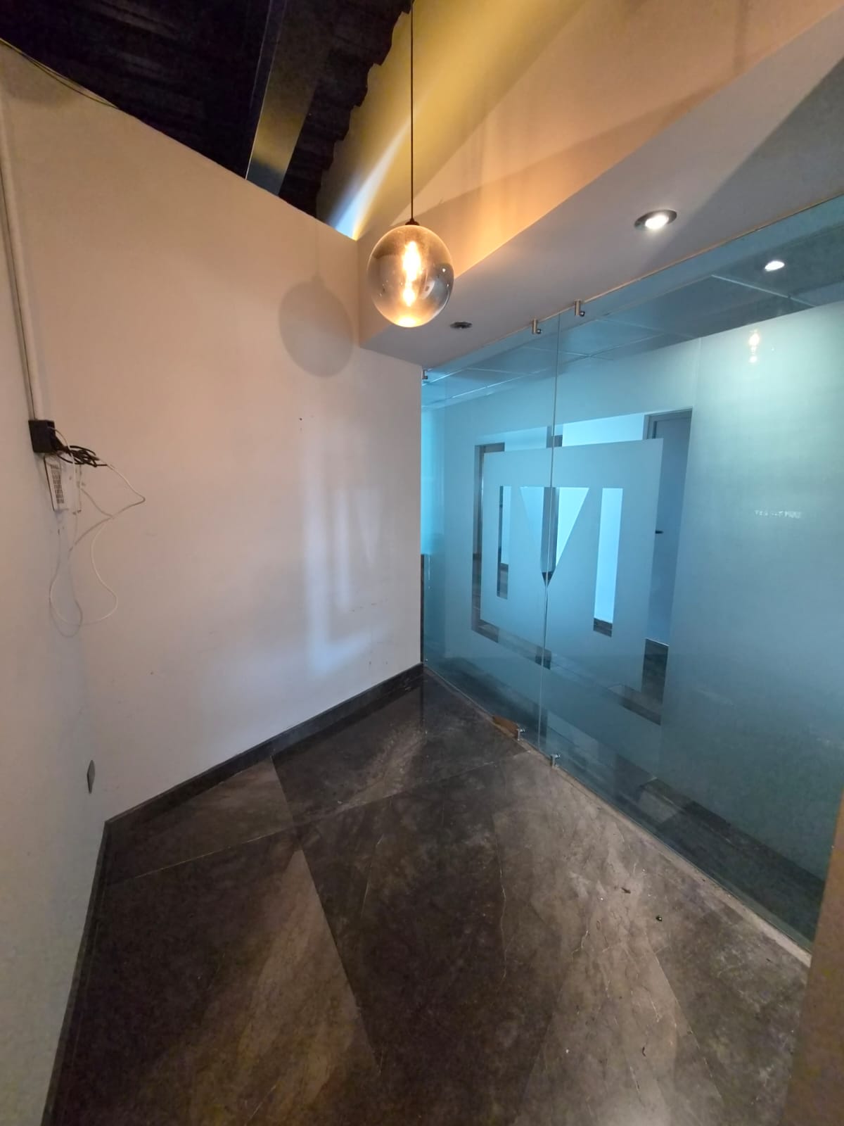 Empty office entrance with a frosted glass partition, dark stone flooring, and a globe pendant light.