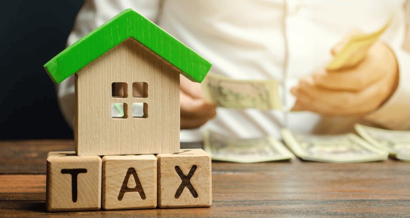 Model house with green roof above TAX blocks as hands count cash.