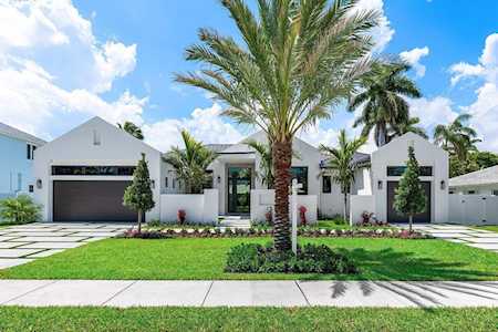 Modern white home with two dark garage doors, a central glass entry, and palm trees across the lawn.