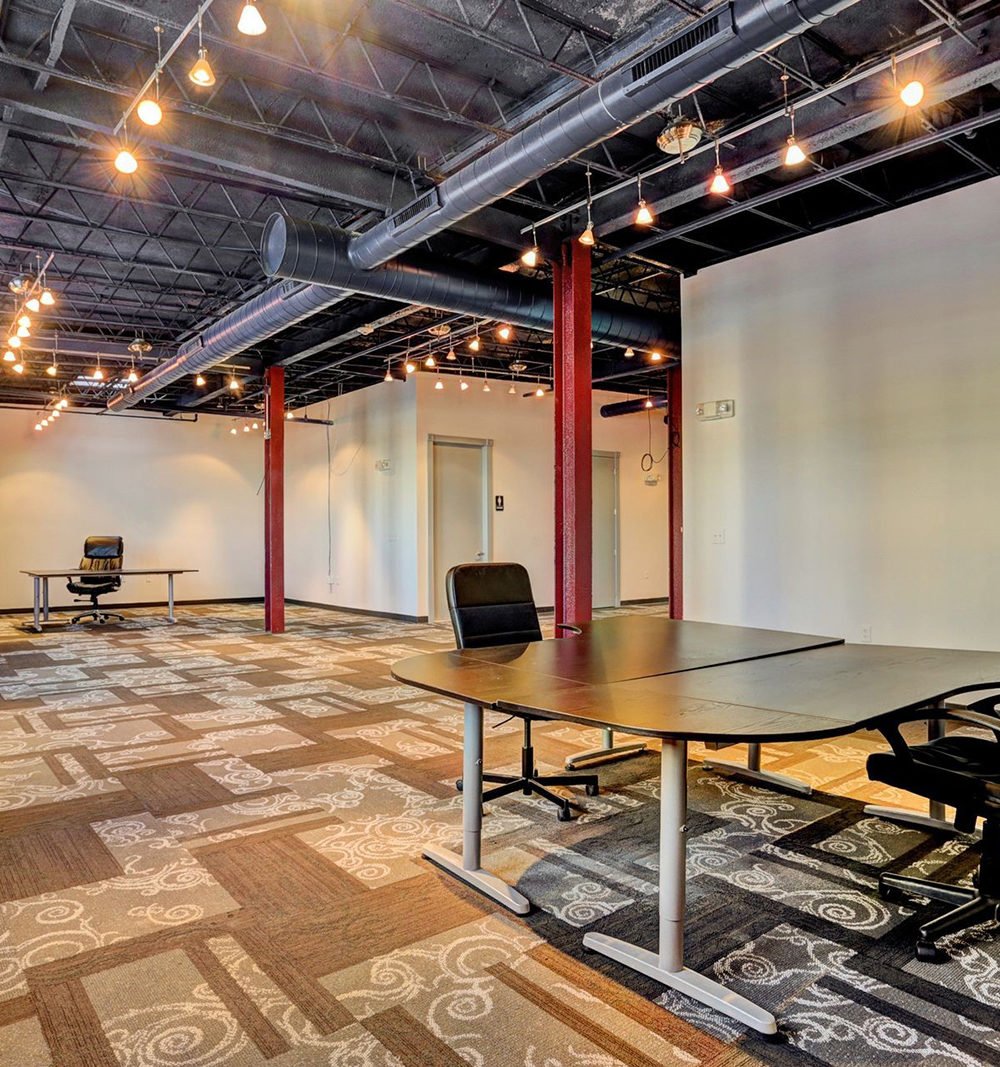 Office with conference tables, patterned carpet, red columns, and exposed ceiling ducts.