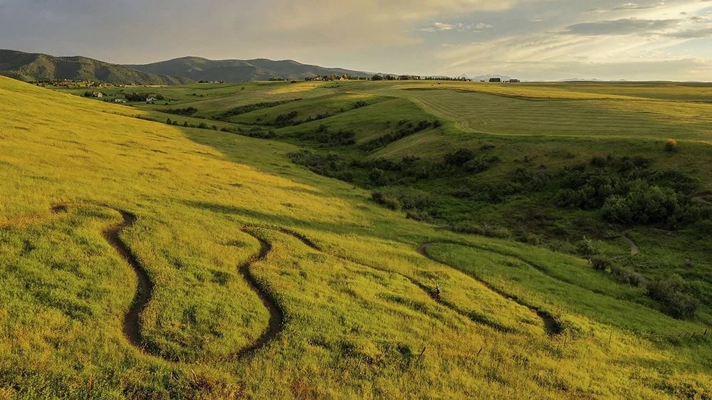 Rolling golden-green hills with winding paths and distant mountain ridges.