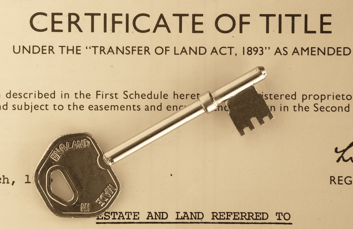 A metal key rests across a certificate of title document.