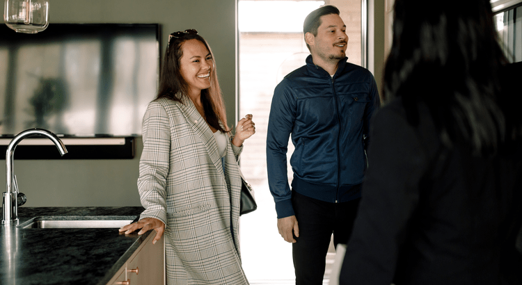 A couple converses with a real estate agent in a modern kitchen, discussing potential home options and features.