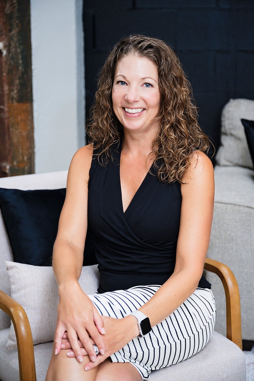 Paula Banatt seated and smiling, wearing a black top and striped skirt.