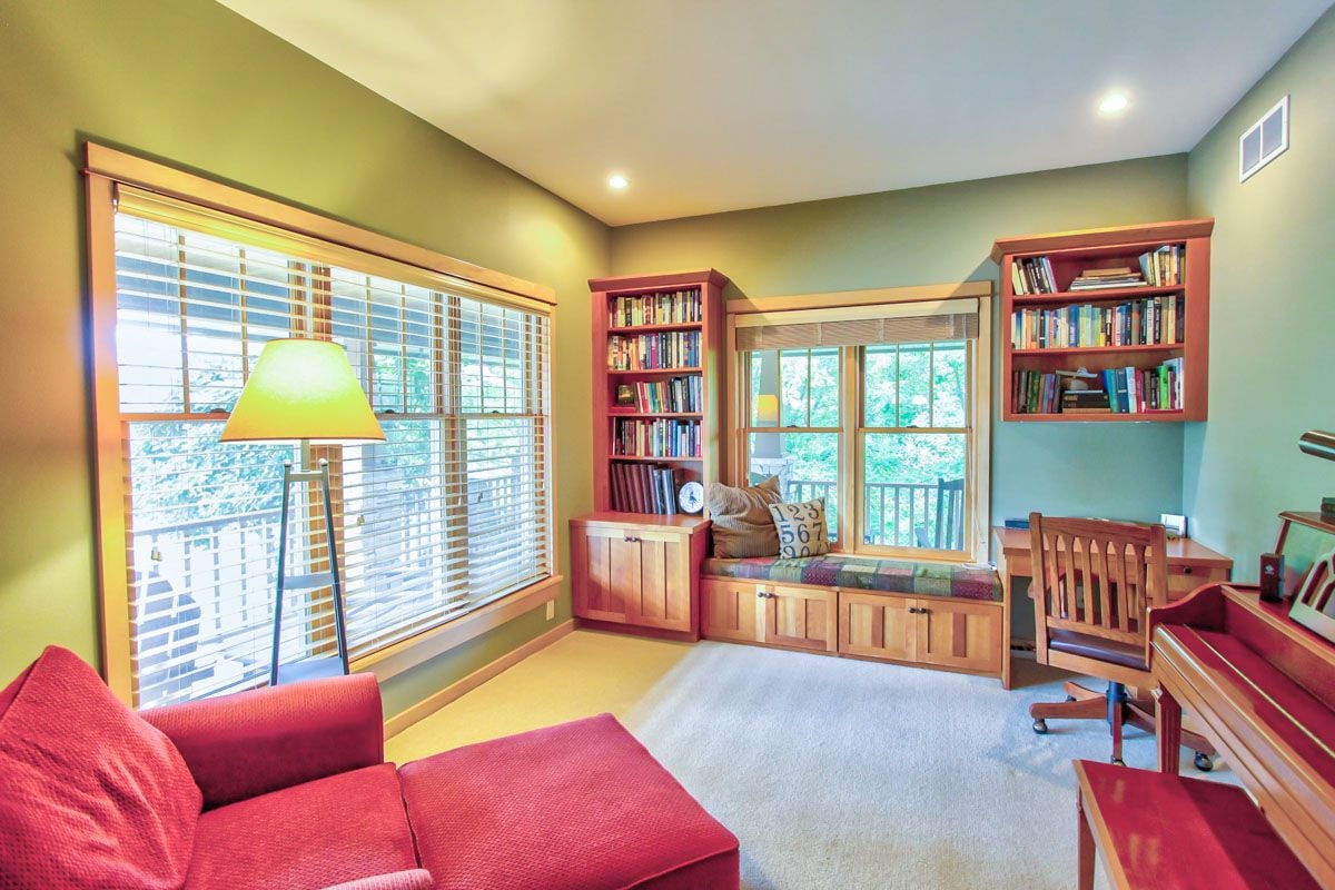Home office with built-in bookshelves, a window seat, and a red sectional sofa.