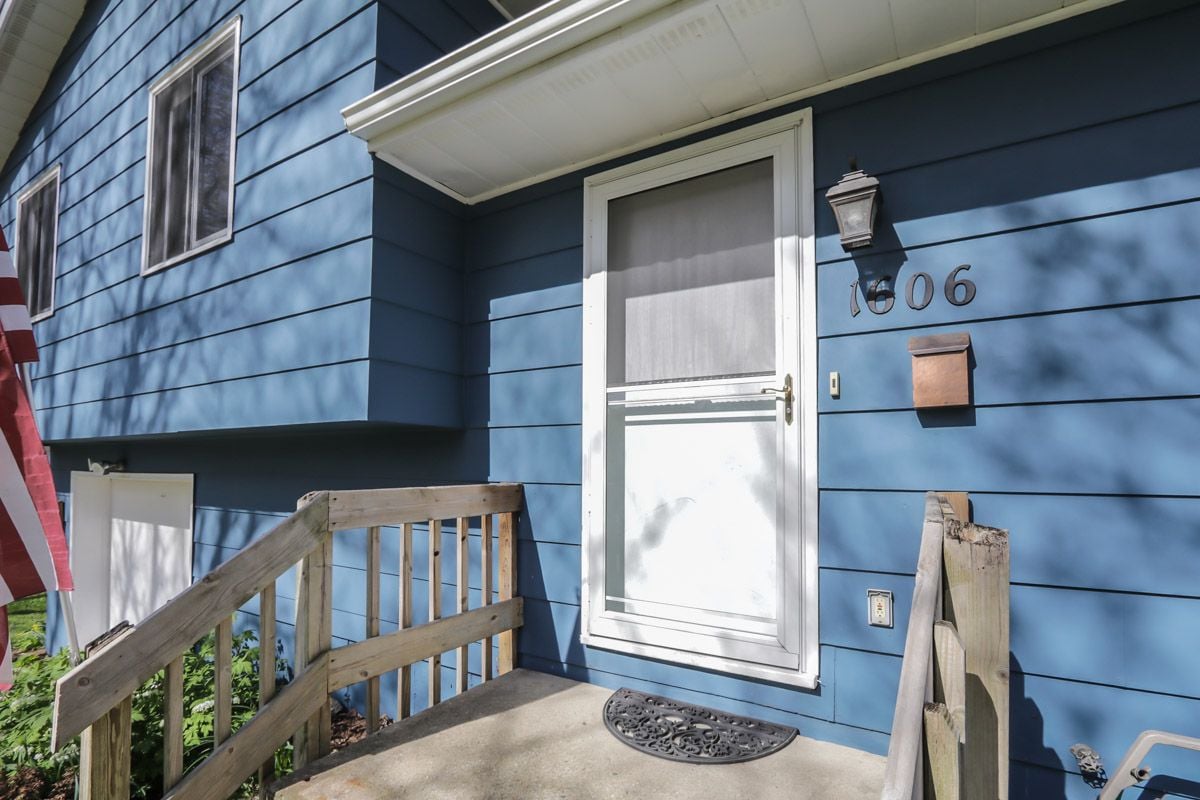 Blue house entrance with white storm door, wooden porch railings, mailbox, and number 1606.