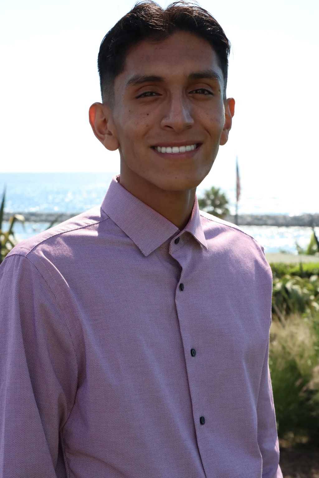 Eros Cortes smiling in a lavender button-down shirt by the water.