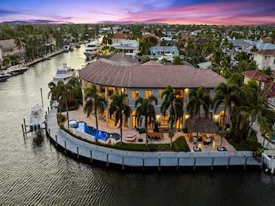 Waterfront home on a canal with a swimming pool, palm-lined grounds, and private dock at dusk.