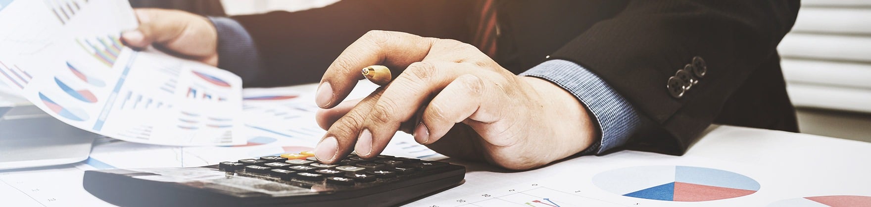 Person calculating figures with a calculator beside financial charts and paperwork.