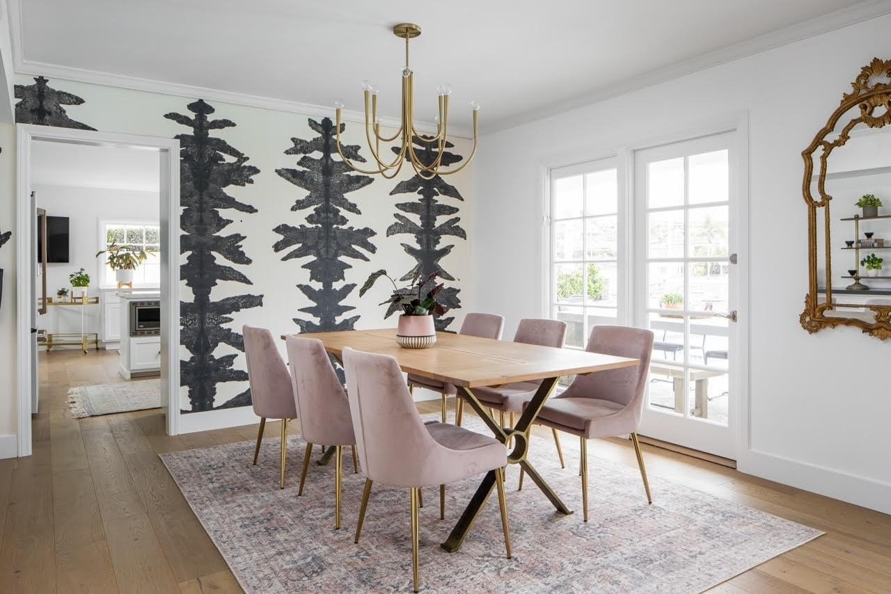  A chic dining room with a wooden table, blush pink velvet chairs, and a striking black and white patterned accent wall.