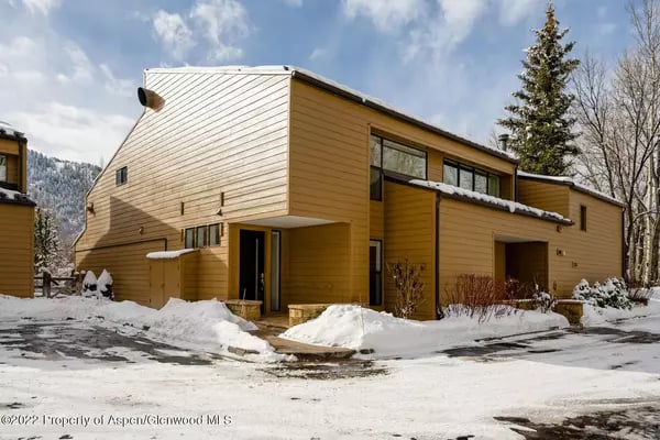 Modern wood-sided home with angular rooflines, surrounded by snow, with a mountain in the background.