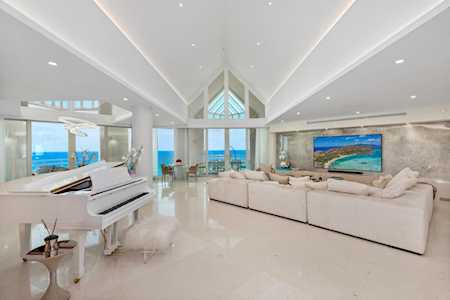 Living room with a white grand piano, vaulted ceiling, and large windows overlooking the water.