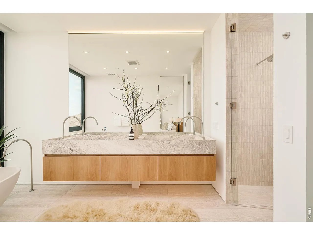 Modern bathroom with a floating wood vanity, pale stone counter, large mirror, and tiled glass shower.