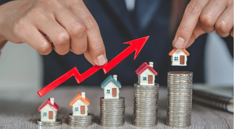 Miniature houses on rising stacks of coins beneath a red upward arrow.