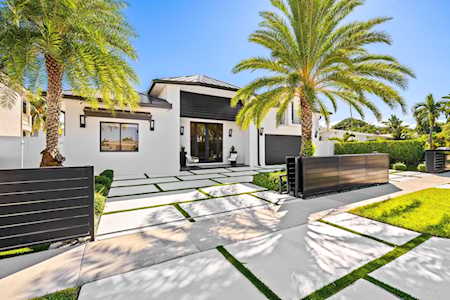 Modern white home with dark trim, palm trees, and a geometric paved driveway.