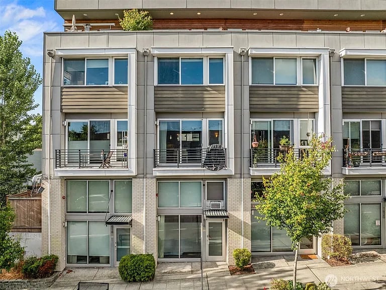 Modern townhouse facade with large windows, small balconies, and landscaped sidewalk.