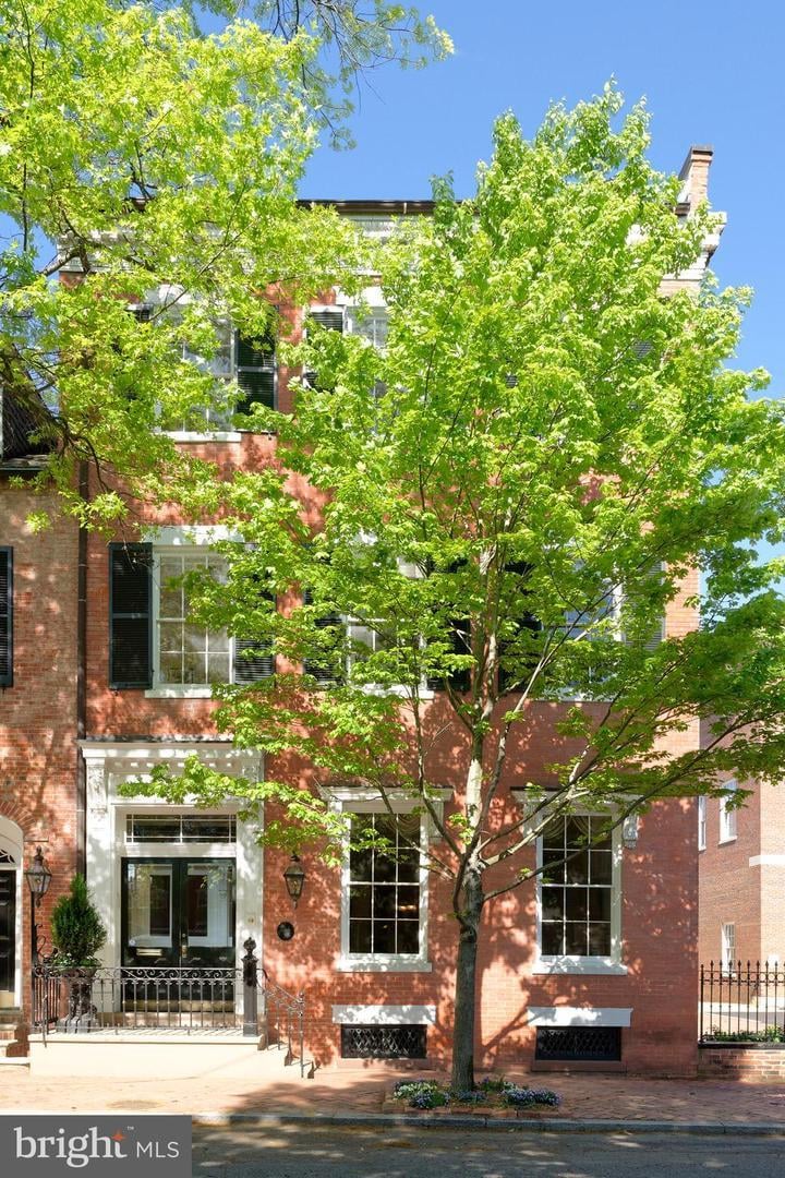 Red-brick townhouse behind a leafy street tree, with white-trimmed windows and an iron entry railing.