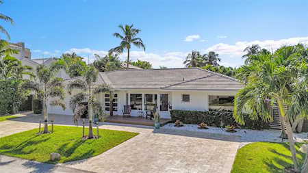 Single-story home with a tiled roof, covered porch, paved driveway, and palm-lined lawn.