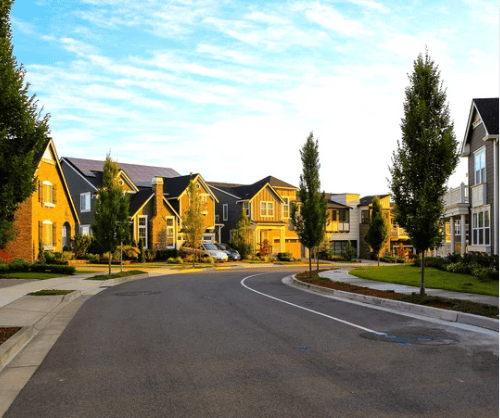 Modern homes line a curved neighborhood street with landscaped lawns and mature trees.