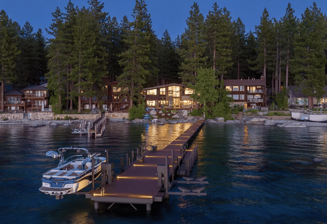 Lakefront homes glow at dusk behind a long dock and moored motorboat.