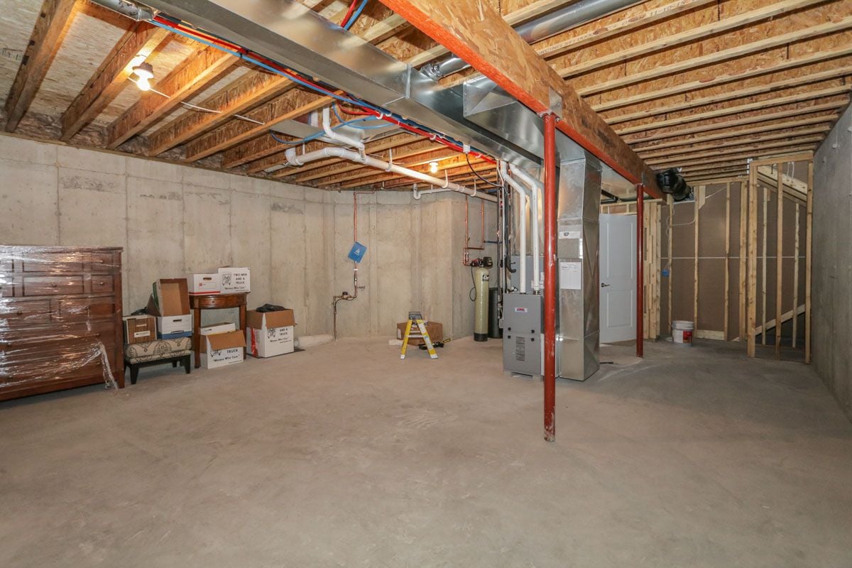 Unfinished basement with exposed ceiling joists, HVAC equipment, and stored boxes.