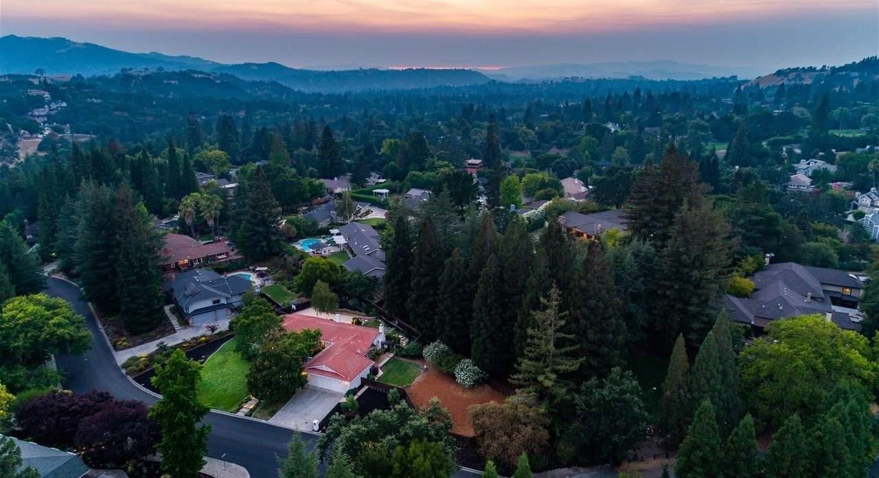 Aerial view of tree-lined homes and rolling hills at dusk.