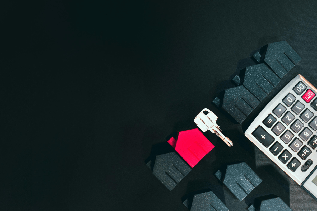 A set of house miniatures, a red keychain, and a calculator on a black background representing real estate market analysis in Victoria, BC.