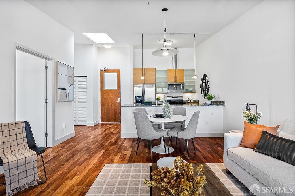 Open-plan living room with hardwood floors, a dining table, and a kitchen breakfast bar.