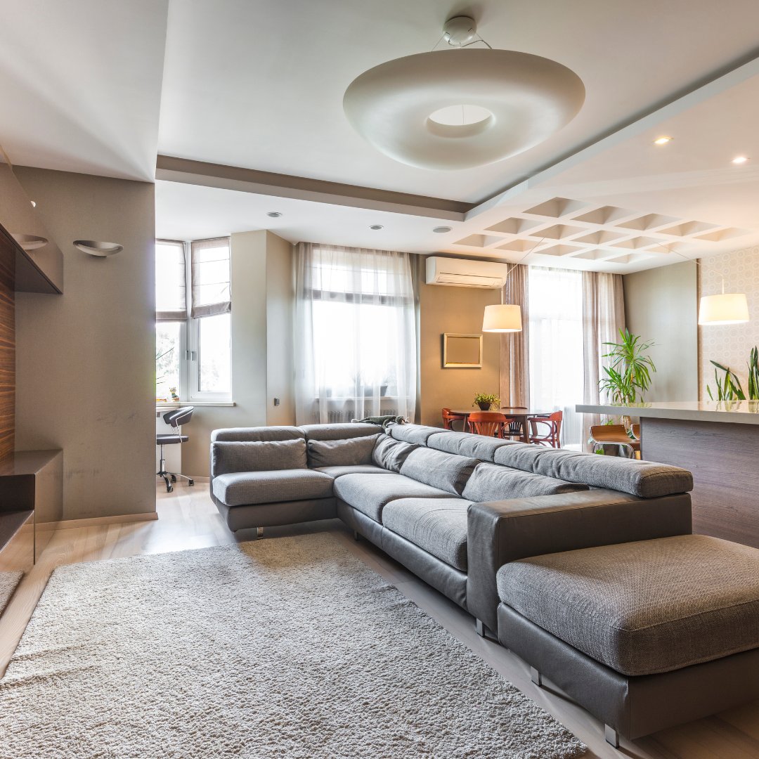 Living room with a gray sectional, large rug, tall curtained windows, and sculptural ceiling light.